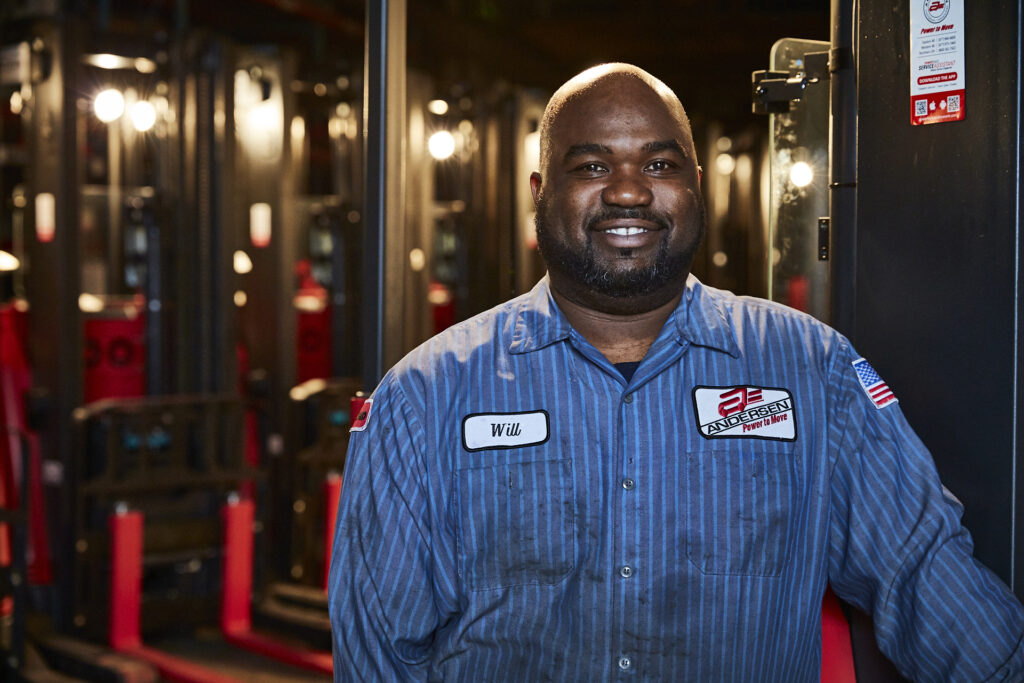 Will, an employee at Andersen Forklift, smiling in his work uniform, captured by Visionary Headshots.